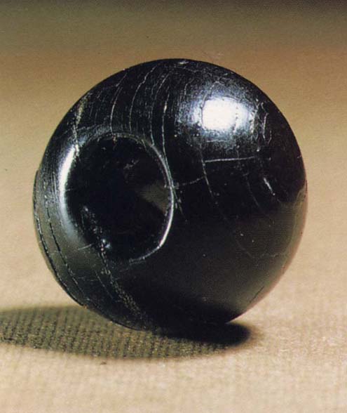 A photograph of a spherical black bead with a central perforation